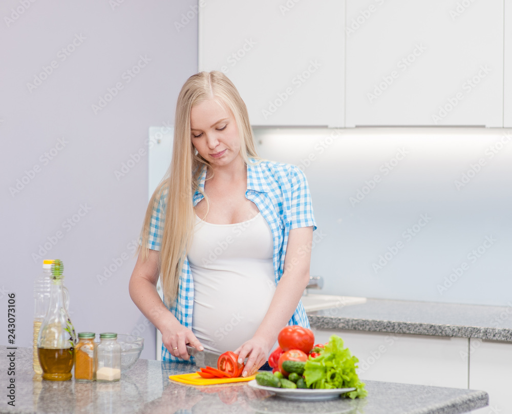 Young pregnant woman at kitchen prepares a vegetable salad Young pregnant woman at kitchen prepares a vegetable salad