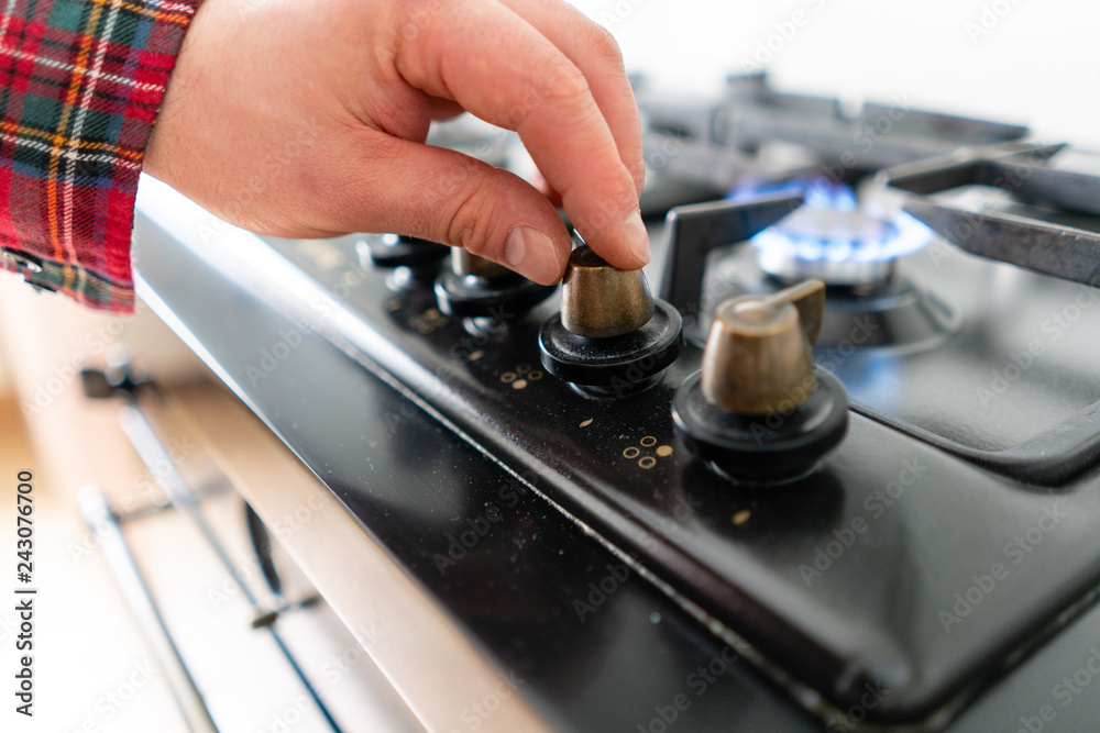 A man lighting the gas-stove with by means of automatic electric ignition. Modern gas burner and hob on a kitchen range. Dark black color and wooden Small kitchen in a modern apartment A man lighting the gas-stove with by means of automatic electric ignition. Modern gas burner and hob on a kitchen range. Dark black color and wooden Small kitchen in a modern apartment