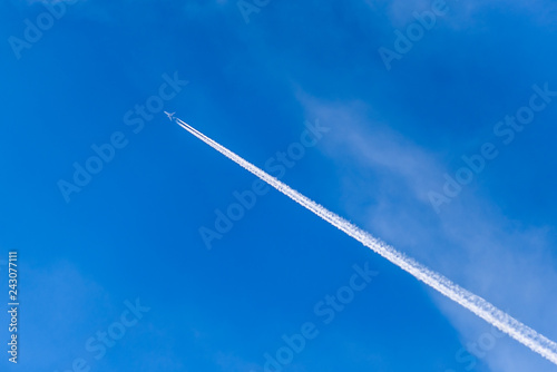 Photography A distant aircraft with long diagonal condensation trails or contrails on a blue