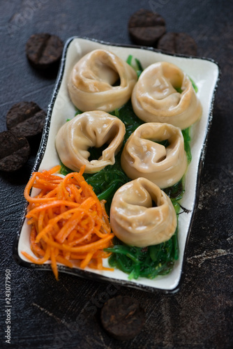 Plate with steamed asian dumplings, seaweed and carrot salad, studio shot, selective focus