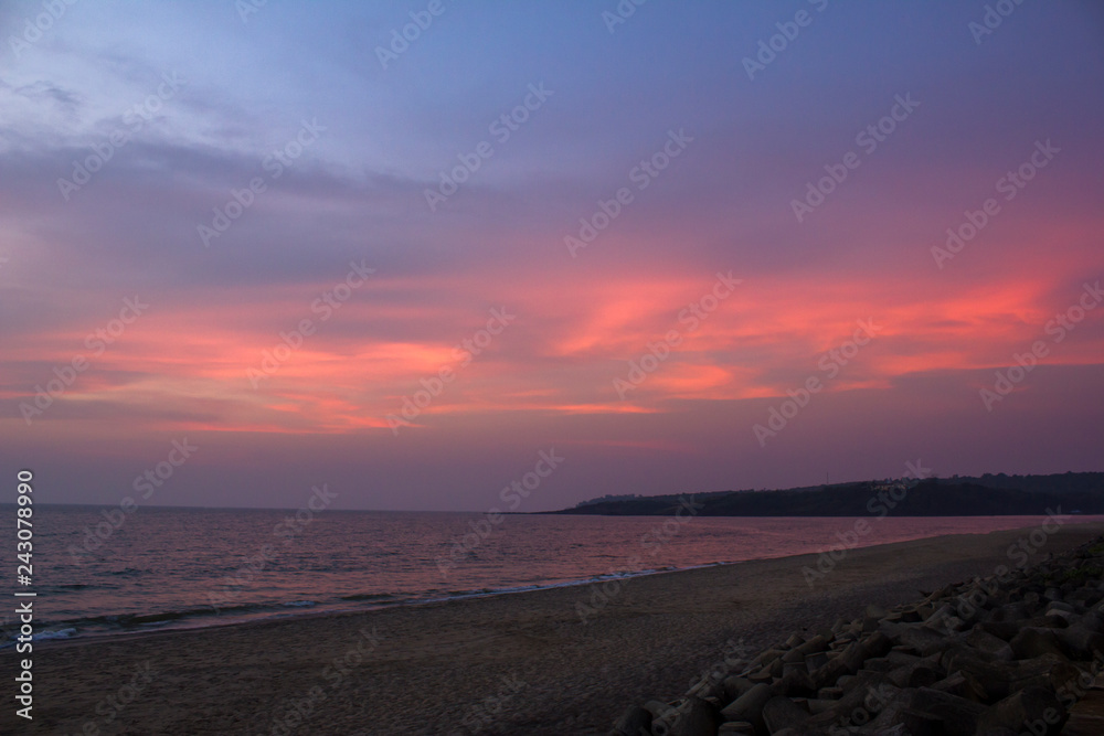 pink clouds in the blue purple sky against the background of the evening sea and sandy beach
