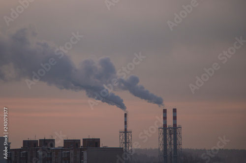 the chimneys of a refinery with smoke and steam with the pink and yellow sunset on the background.