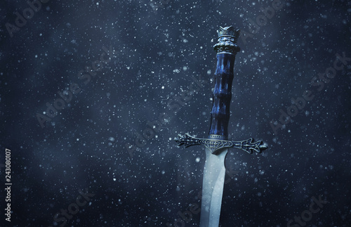 mysterious and magical photo of silver sword over gothic snowy black background. Medieval period concept. photo