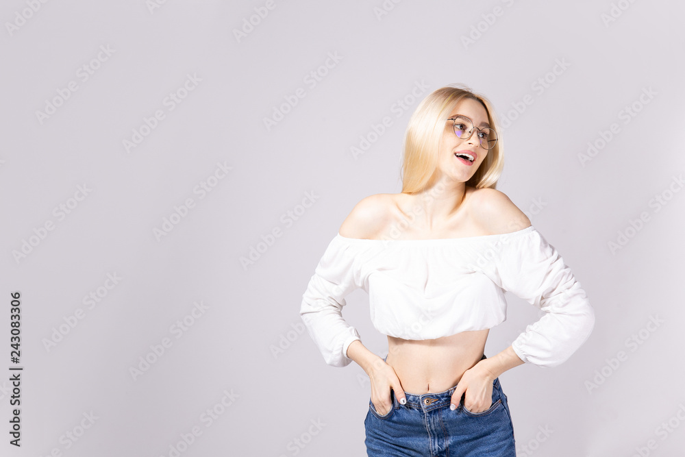 Studio shot of gorgeous young blonde woman with straight hair wearing off shoulder crop top sweater and high waisted denim shorts. Gray isolated background, copy space, close up. Studio shot of gorgeous young blonde woman with straight hair wearing off shoulder crop top sweater and high waisted denim shorts. Gray isolated background, copy space, close up.