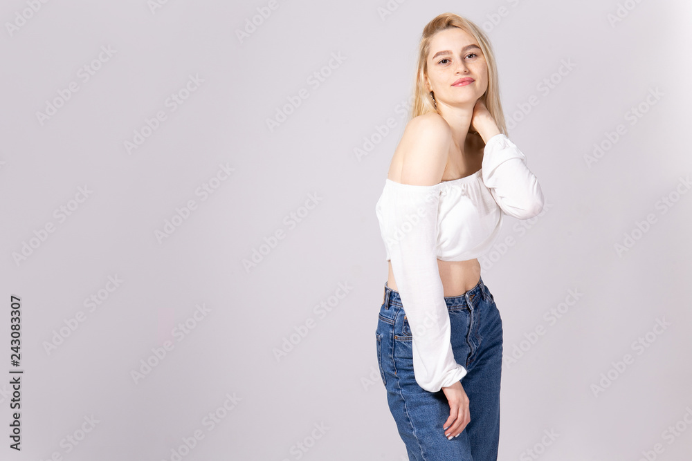 Studio shot of gorgeous young blonde woman with straight hair wearing off shoulder crop top sweater and high waisted denim shorts. Gray isolated background, copy space, close up. Studio shot of gorgeous young blonde woman with straight hair wearing off shoulder crop top sweater and high waisted denim shorts. Gray isolated background, copy space, close up.