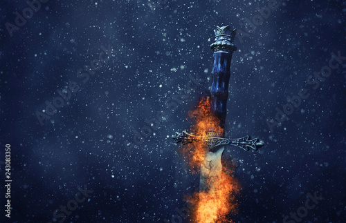 mysterious and magical photo of silver sword with fire flames over gothic snowy black background. Medieval period concept.