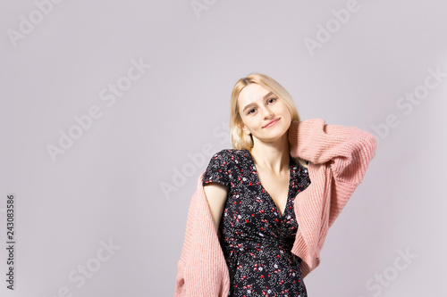 Studio shot of gorgeous young blonde woman with long straight hair wearing soft pink loose knit oversized sweater and feminine black dress. Gray isolated background, copy space, close up, portrait.
