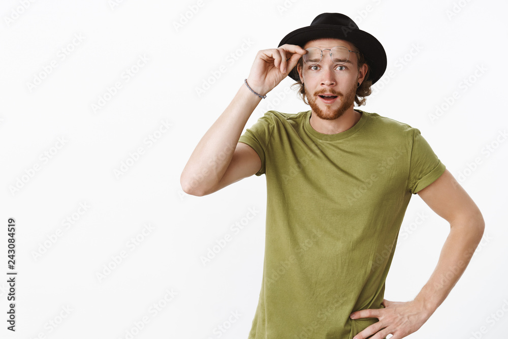 Look what we have here. Portrait of intrigued and interested cute charismatic boyfriend with beard in hat taking off glasses as seeing curious thing looking at camera surprised over gray background Look what we have here. Portrait of intrigued and interested cute charismatic boyfriend with beard in hat taking off glasses as seeing curious thing looking at camera surprised over gray background