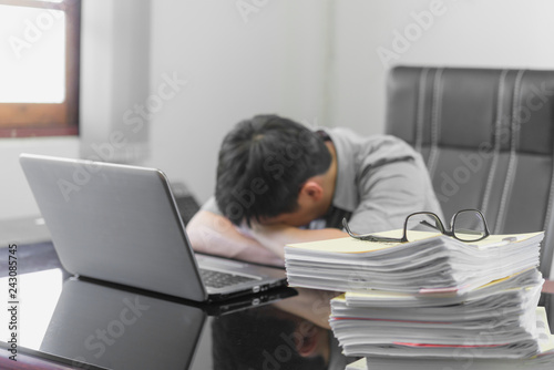 Businessman asleep at office desk with finance sheet calculator, he is having a bad headache, stress and overwork concept.