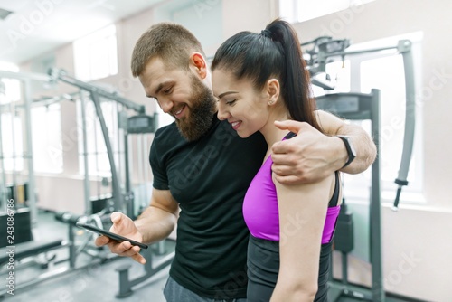 Young woman talking with personal trainer in gym  looking in smartphone and discussing. Fitness  sport  training  people  healthy lifestyle concept