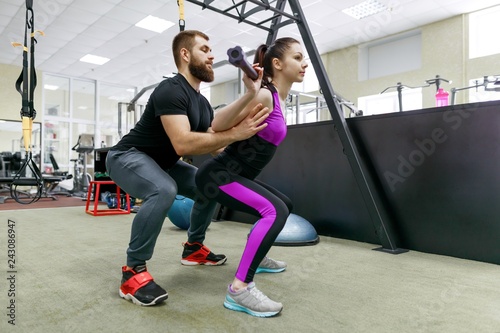 Fototapeta Naklejka Na Ścianę i Meble -  Personal fitness trainer coaching and helping client woman making exercise in gym. Sport, teamwork, training, people concept