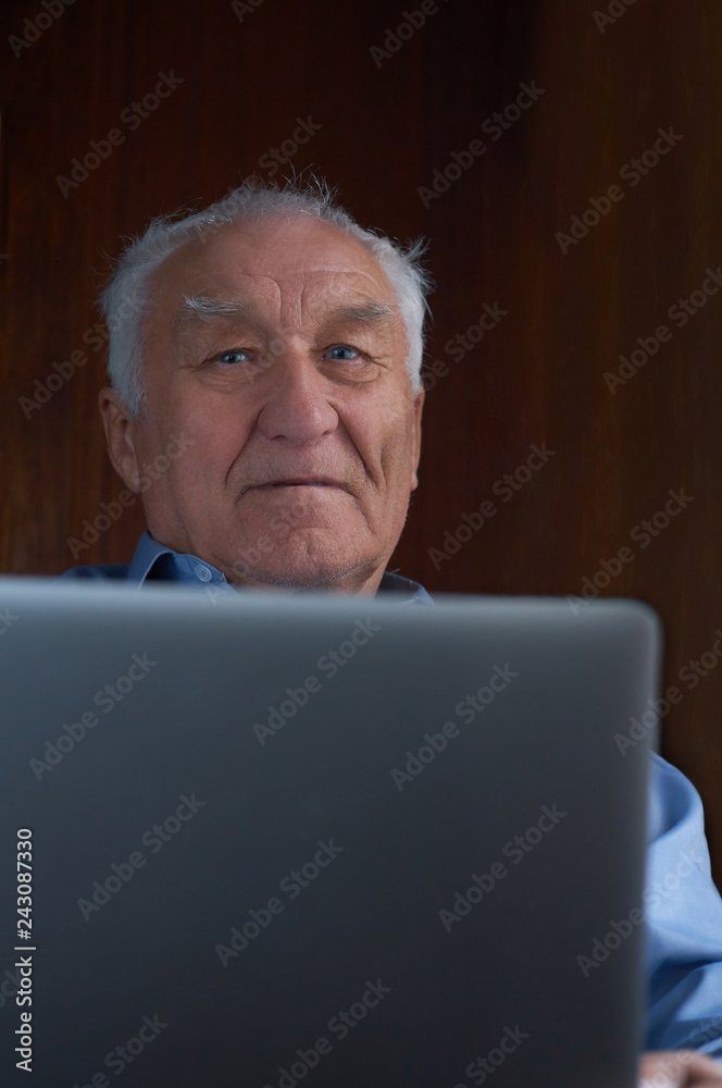 Senior grey-haired man using a laptop sitting in chair at home. Senior grey-haired man using a laptop sitting in chair at home.