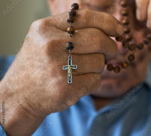 Praying old man with hands holding rosary beads.
