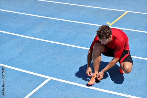 Athlete sprinter getting ready to run tying up shoe laces on stadium running tracks. Man runner preparing for race marathon training outdoors. Fitness and sports.