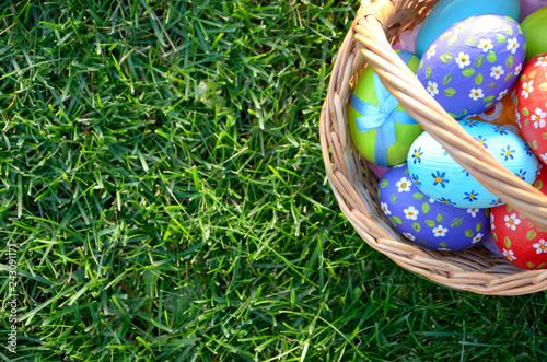 Flat lay shot of Easter eggs in the wicker basket on green spring grass. Space for text
