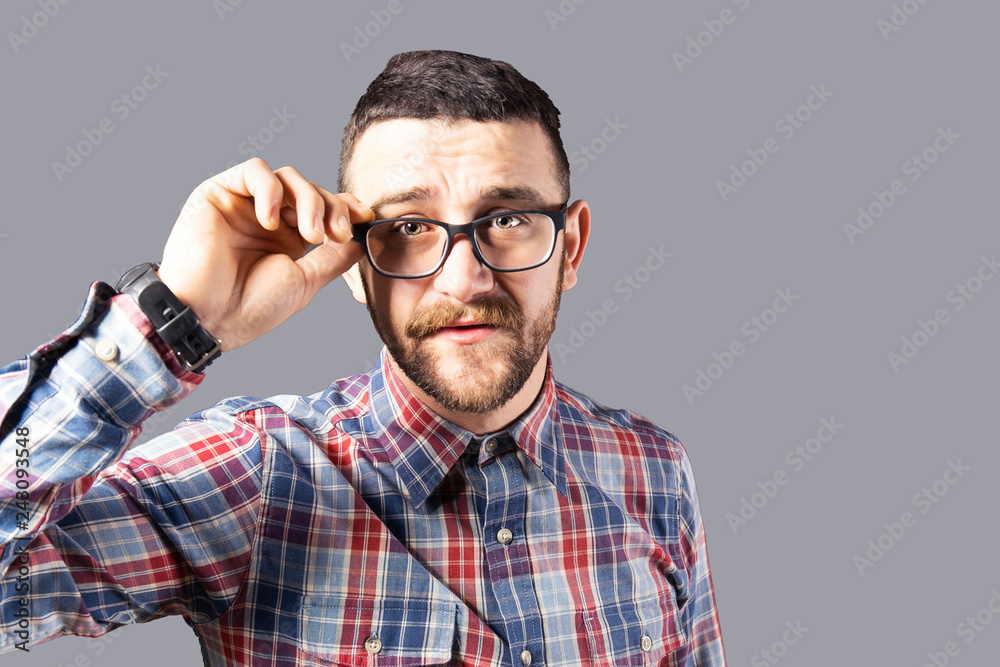 Obraz premium Young handsome man with facial hair holding posing over gray wall with a lot of copy space for text. Portrait of confident bearded male, wearing hipster slim fit checkered shirt. Isolated, background.