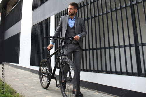 Confident young businessman standing with bicycle on the street in town.