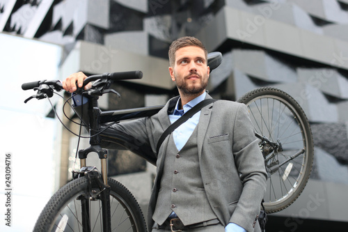 Confident young businessman carrying his bicycle while walking outdoors.