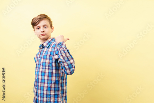 confident boy pointing to object or text behind his back. advertisement or product placement, banner or poster template, emotion facial expression, people reaction