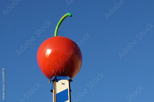  Big red artificial cherry on the blue sky background