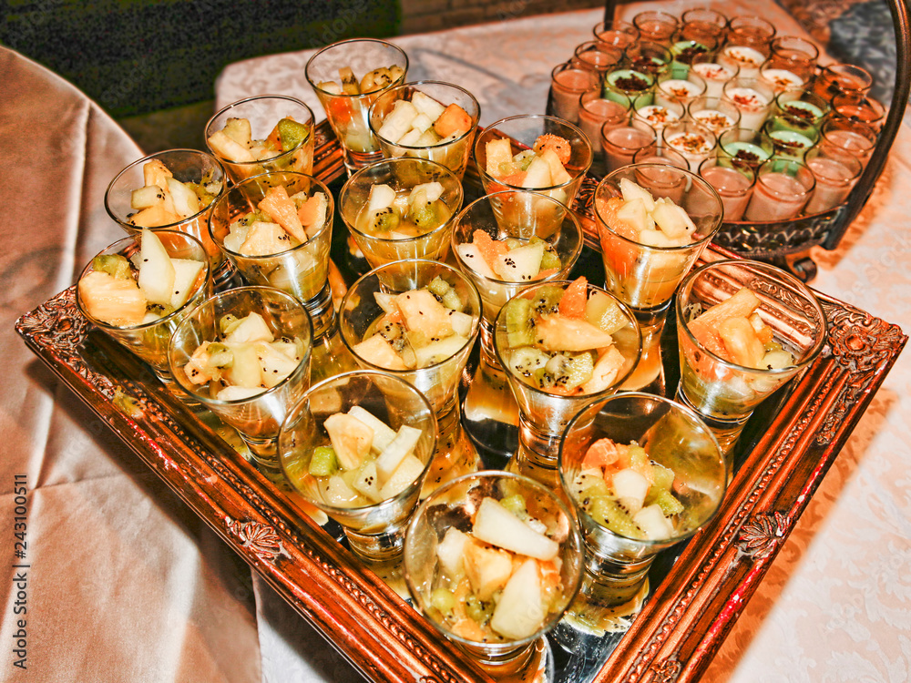Several dessert glasses with fruit salad laid on a mirror decorative tray