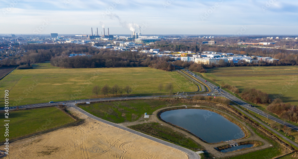 Aerial view of a rainwater retention basin with roads and a large meadow area and an industrial city in the background