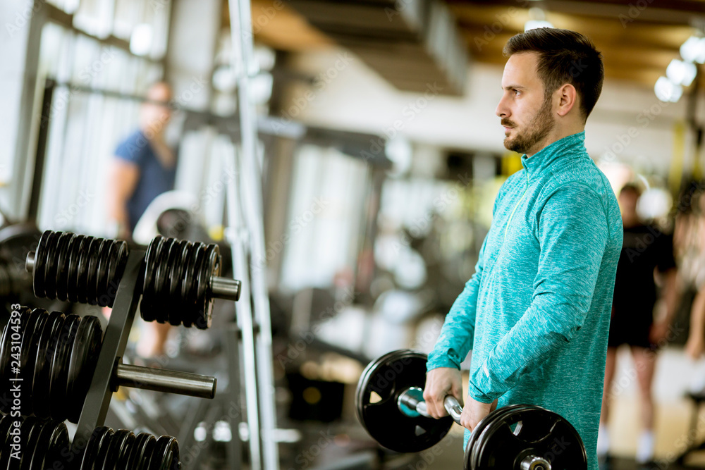 Handsome young man uses dumbbells in gym Handsome young man uses dumbbells in gym