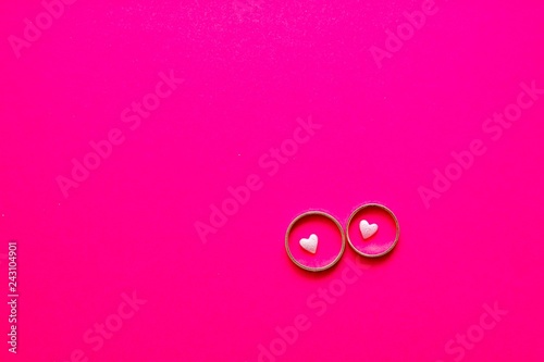 Love and marriage concept. Valentine's Day. Two golden wedding rings with small light pink hearts within on bright pink background with copy space