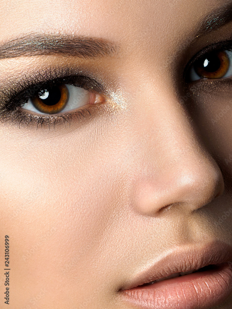 Naklejka premium Close up beauty portrait of young woman with golden makeup. Perfect skin and fashion makeup, smokey eyes. Studio shot. Sensuality, passion and skincare concept. Extreme closeup, partial face view