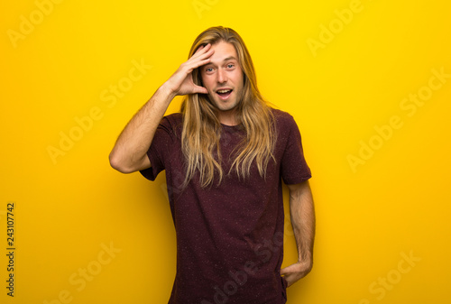 Blond man with long hair over yellow wall has just realized something and has intending the solution