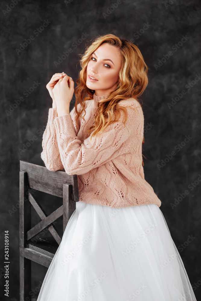 Studio shot of beautiful young woman with blonde hair wearing loose long-sleeved sweater over white dress. Beauty and youth Studio shot of beautiful young woman with blonde hair wearing loose long-sleeved sweater over white dress. Beauty and youth