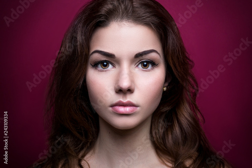 Beautiful girl looking at the camera.Shoot at studio. On a pink background. Strong face. Iris eyes. Portrait young woman. Beauty. Clean skin. Pretty model with curly hairstyle. Adult. Retouching.