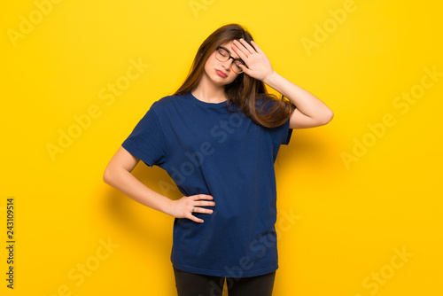 Young woman with glasses over yellow wall with tired and sick expression