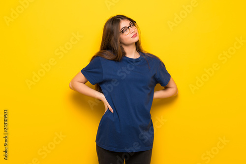 Young woman with glasses over yellow wall suffering from backache for having made an effort © luismolinero