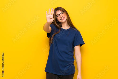 Young woman with glasses over yellow wall happy and counting four with fingers © luismolinero
