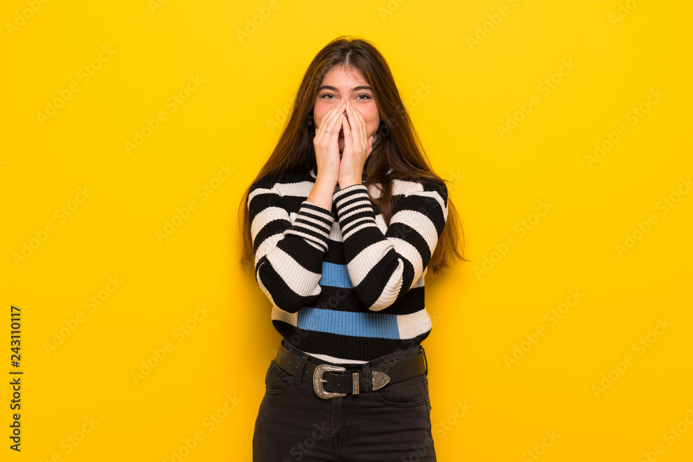 Young woman over yellow wall smiling a lot while covering mouth Young woman over yellow wall smiling a lot while covering mouth
