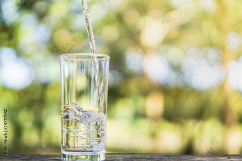 Pouring fresh water on drinking glass over nature background
