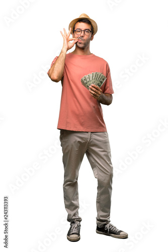 Man holding many bills showing a sign of closing mouth and silence gesture on isolated white background
