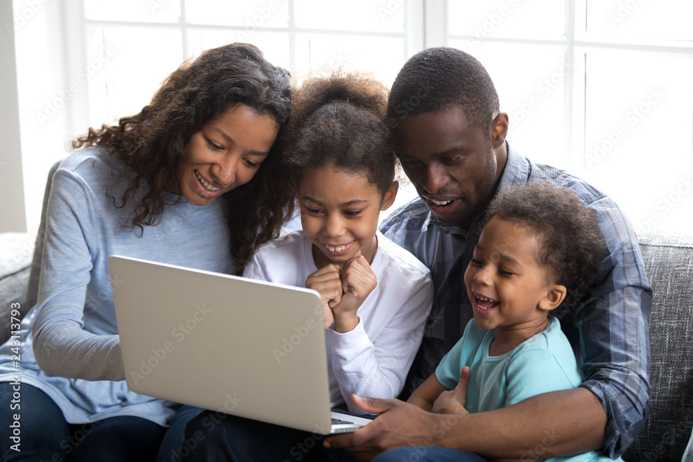 Happy african family with 2 children having fun using laptop together at  home, black parents and little kids watching funny video, doing online  shopping, making video call looking at computer screen Stock
