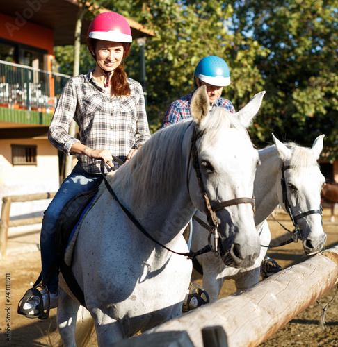 Woman and man in helmets training riding horse at farm at summer day