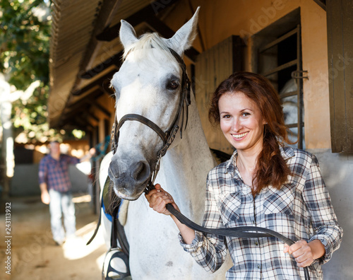 Female farmer standing  with white horse  at stable outdoor