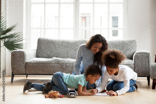 Loving black mom and little mixed race children drawing with colored pencils in living room, happy single african mum helping kids with creative activity at home, underfloor heating, family hobbies photo