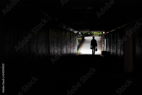 in a dark tunnel silhouette of a walking man  the background of trees and a footpath