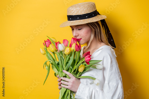 Beautiful woman in white shirt and hat with fresh springtime tulips on yellow background