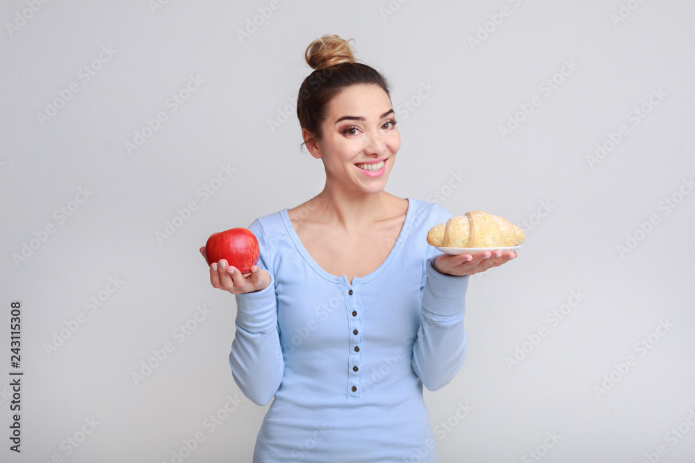 Young woman choosing between croissant and apple