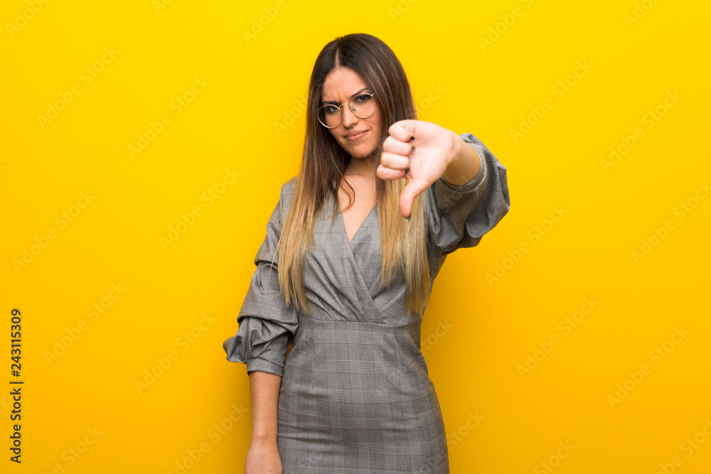 Obraz premium Young woman with glasses over yellow wall showing thumb down sign with negative expression