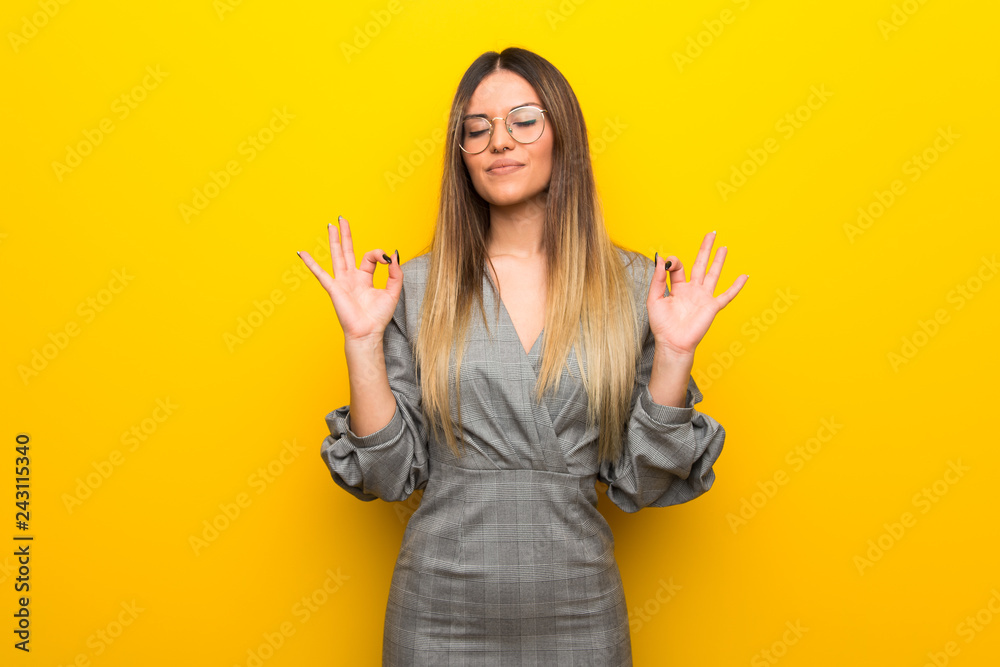 Young woman with glasses over yellow wall in zen pose Young woman with glasses over yellow wall in zen pose
