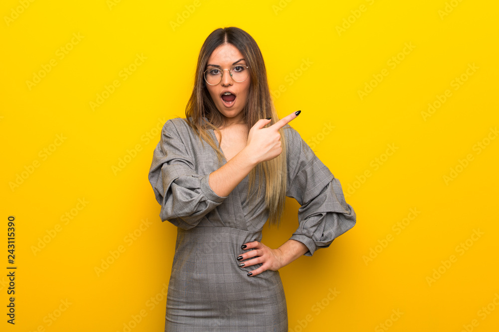 Young woman with glasses over yellow wall surprised and pointing side
