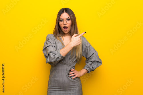 Young woman with glasses over yellow wall surprised and pointing side © luismolinero