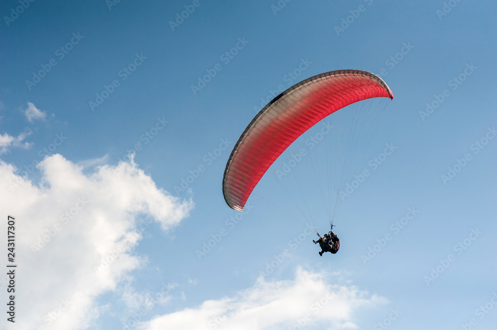 Alone paraglider flying in the blue sky against the background of clouds. Paragliding in the sky on a sunny day. Alone paraglider flying in the blue sky against the background of clouds. Paragliding in the sky on a sunny day.
